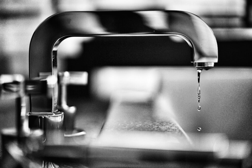 Chrome faucet dripping water over the edge of a sink.